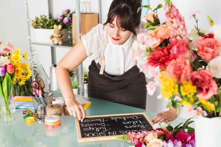 A female florist writing flowers name on a slate with multiple affordable to luxury flower bouquet options around.