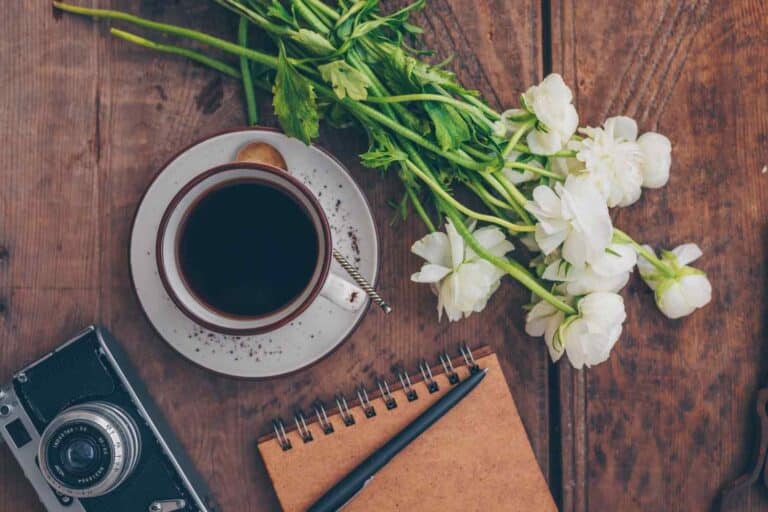 A cup of coffee and a bunch of white flowers placed on a wooden table nicely.