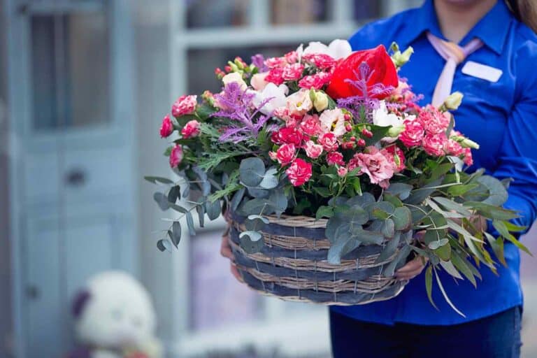 A female flower delivery professional delivering a flower basket to customer.
